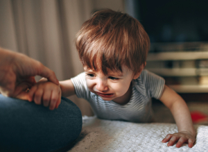 Child crying with hand outstretched to hold a parent's hand, at the edge of a couch